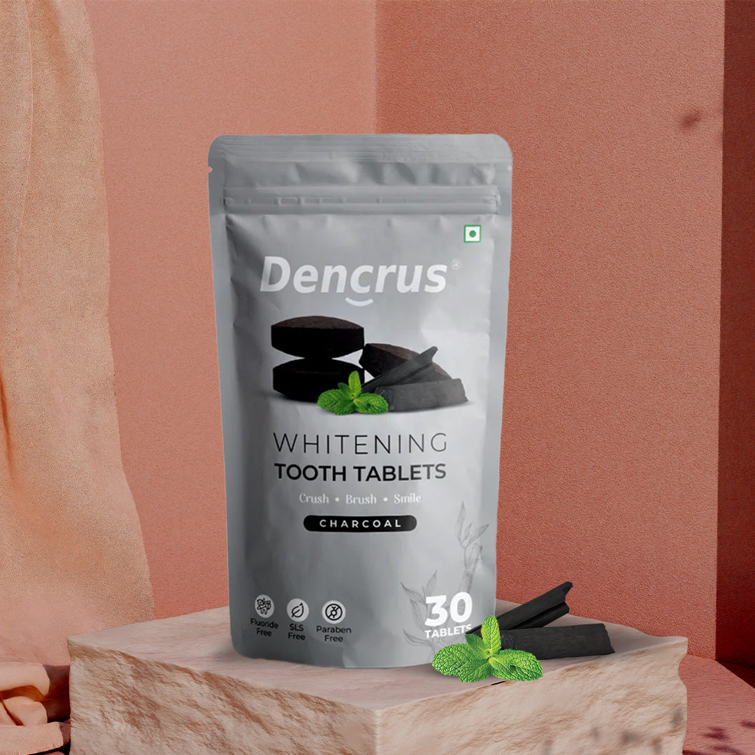 A package of Dencrus whitening tooth tablets with charcoal flavor displayed on a wooden surface with a pink background.