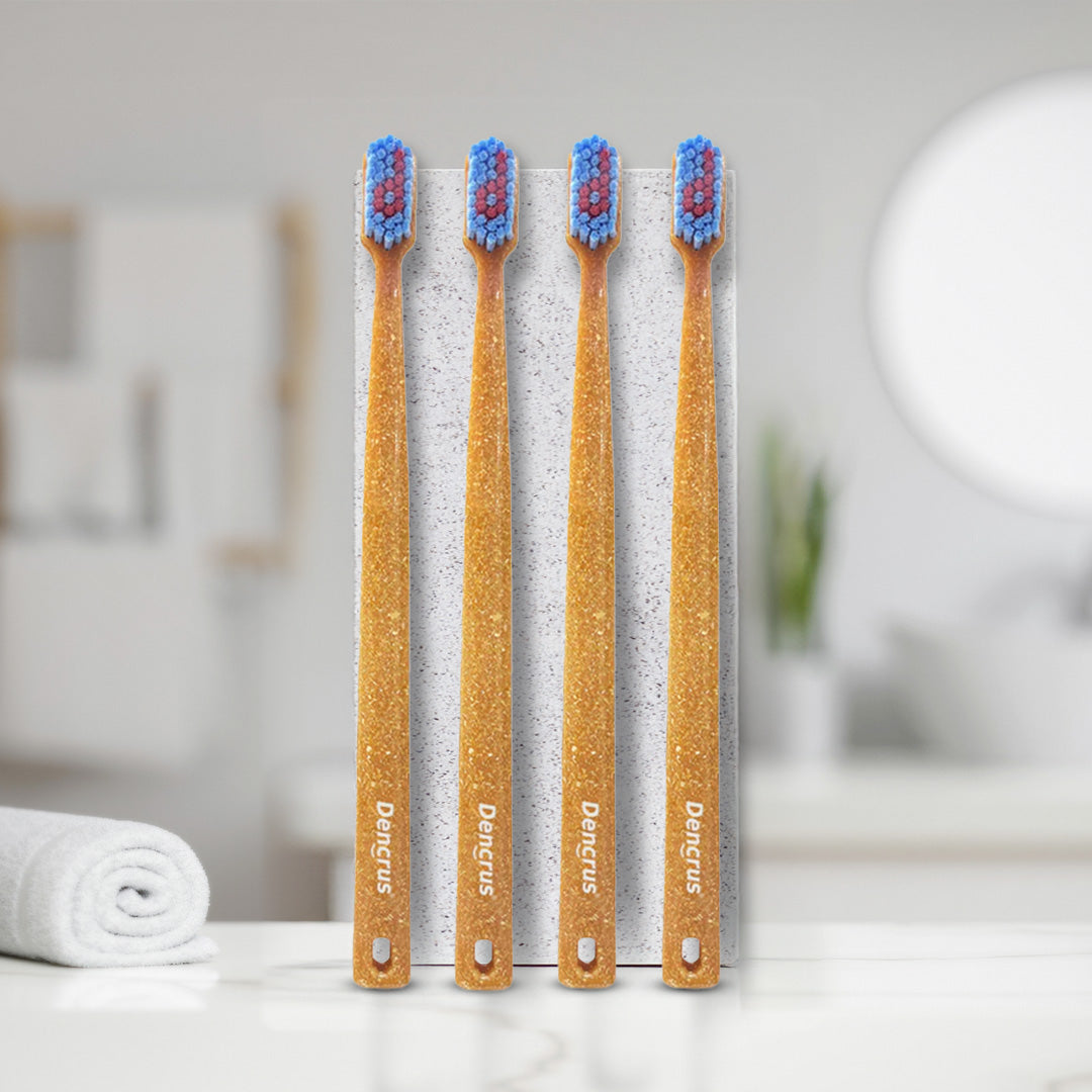 4 bamboo toothbrushes with blue and red bristles, standing upright. They are placed on a bathroom counter.