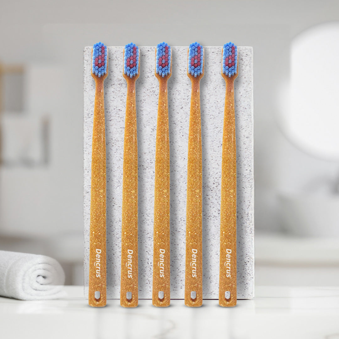 Five bamboo toothbrushes with blue and red bristles that has 'Dencrus' branding labels, placed in front of a white slab.