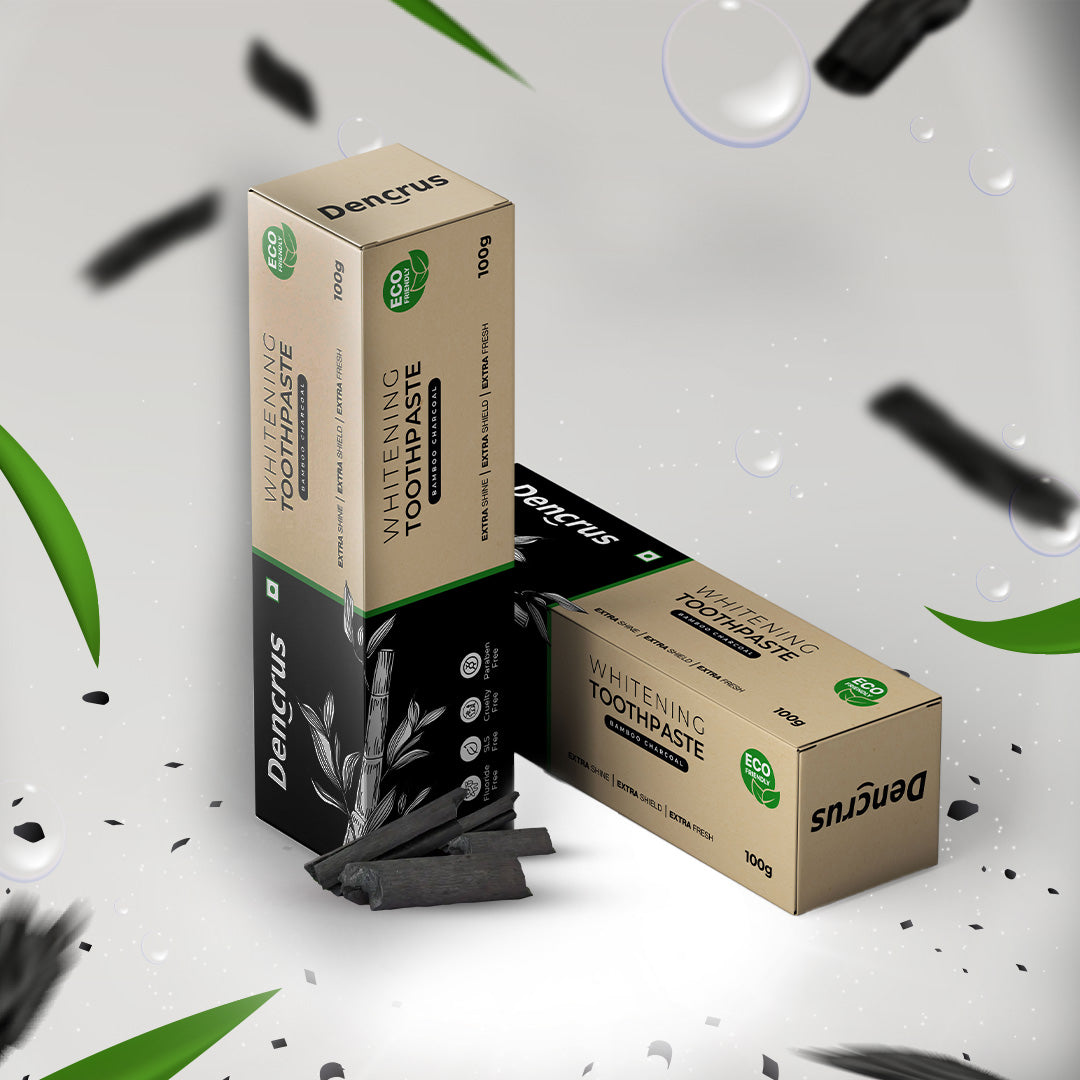 Two packs of Dencrus Bamboo Charcoal Toothpaste presented against a white background with leaves and blurry charcoal particles