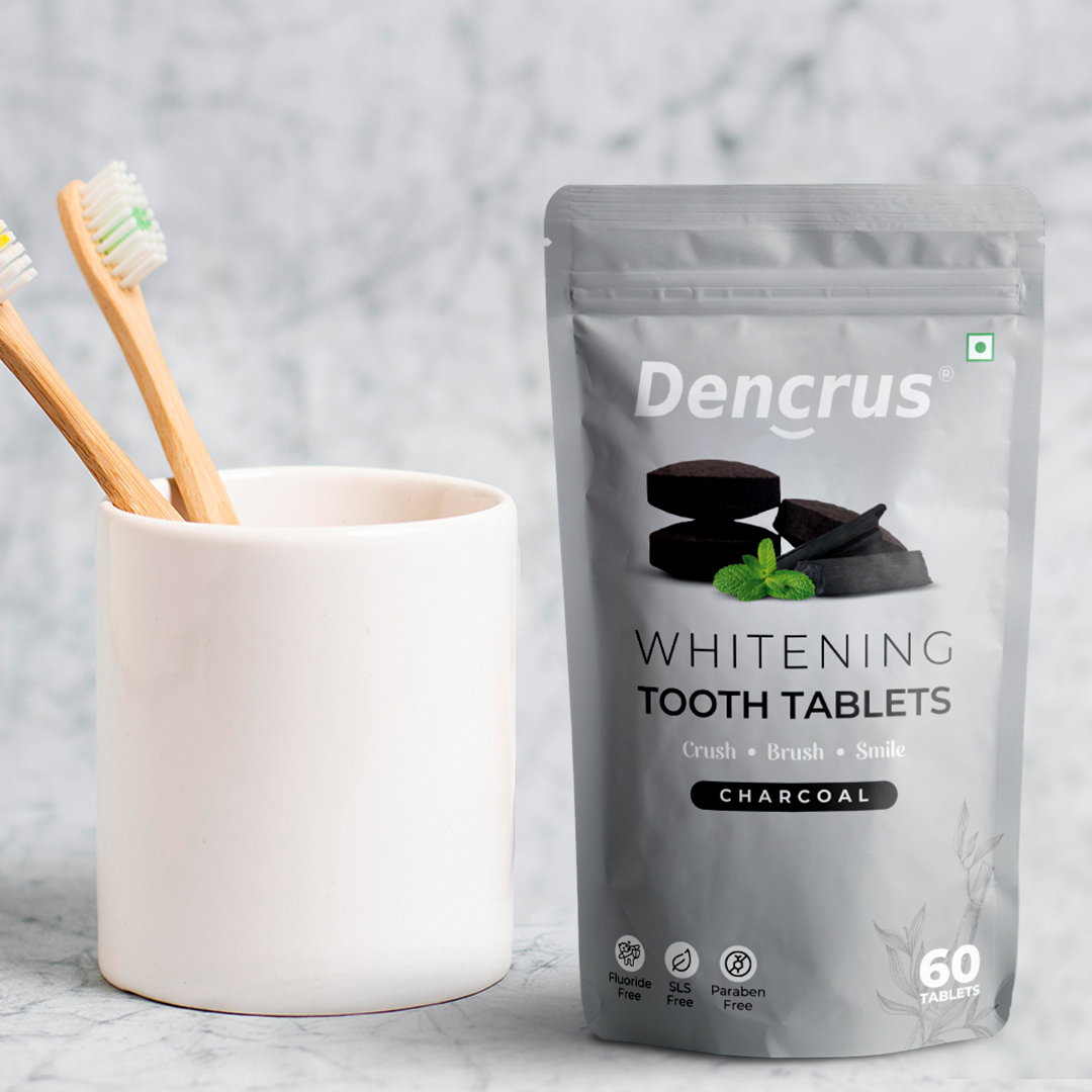 Dencrus whitening tooth tablets with charcoal flavor displayed with two toothbrushes in a cup against a white background
