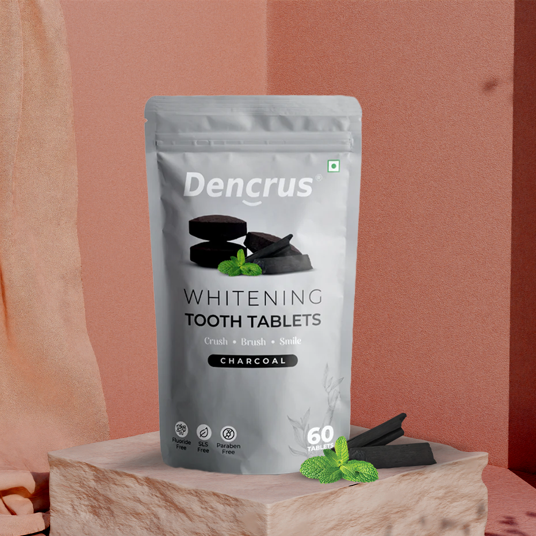 Dencrus whitening tooth tablets with charcoal flavor displayed on a wooden surface with a pink background.