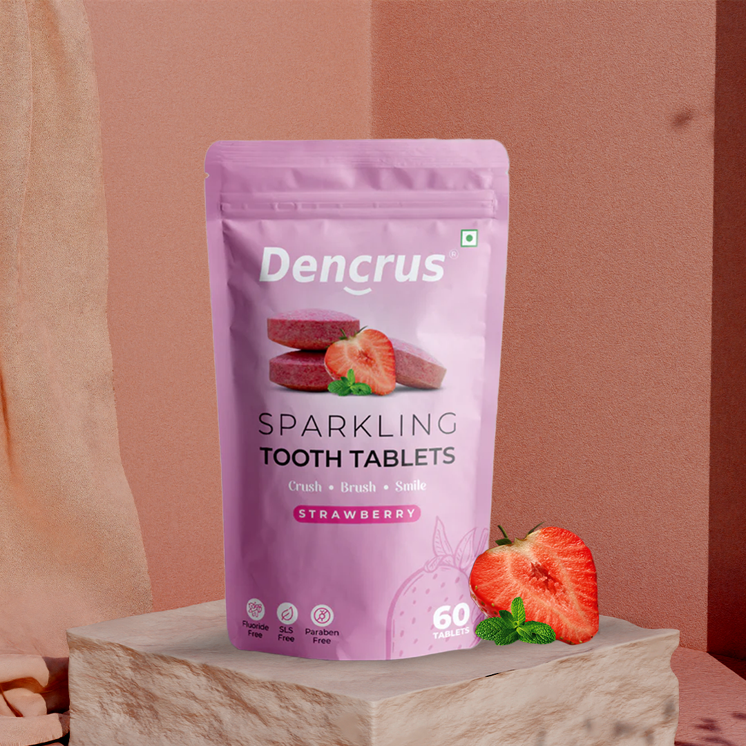 A pink package of Dencrus Sparkling Tooth Tablets with a strawberry flavor, accompanied by an image of a strawberry and a mint leaf on a wooden surface.