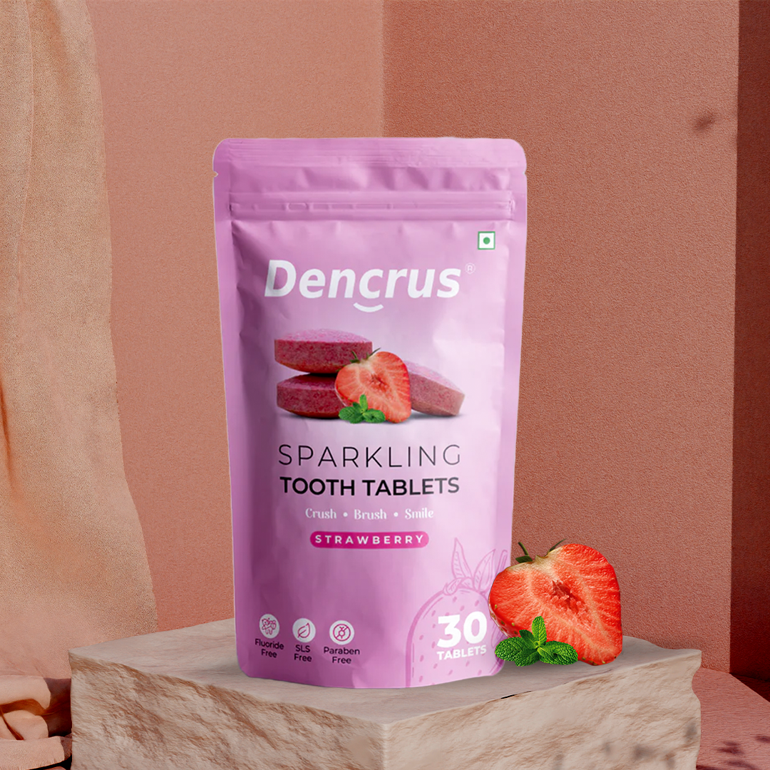 A pink package of Dencrus Sparkling Tooth Tablets with a strawberry flavor, accompanied by an image of a strawberry and a mint leaf on a wooden surface.