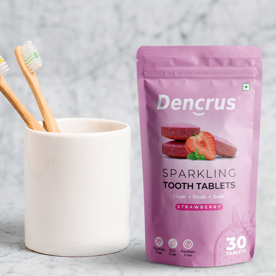 An image of Dencrus Sparkling Strawberry tooth tablets is placed on a white background. Beside there are two toothbrushes are placed on the cup.