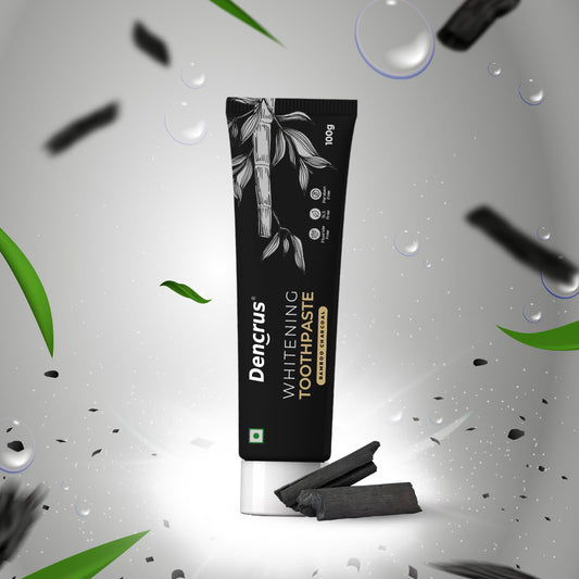 A tube of Dencrus Whitening Toothpaste with charcoal particles visible, presented against a black background with water droplets and leaves accents to highlight its natural and organic qualities.