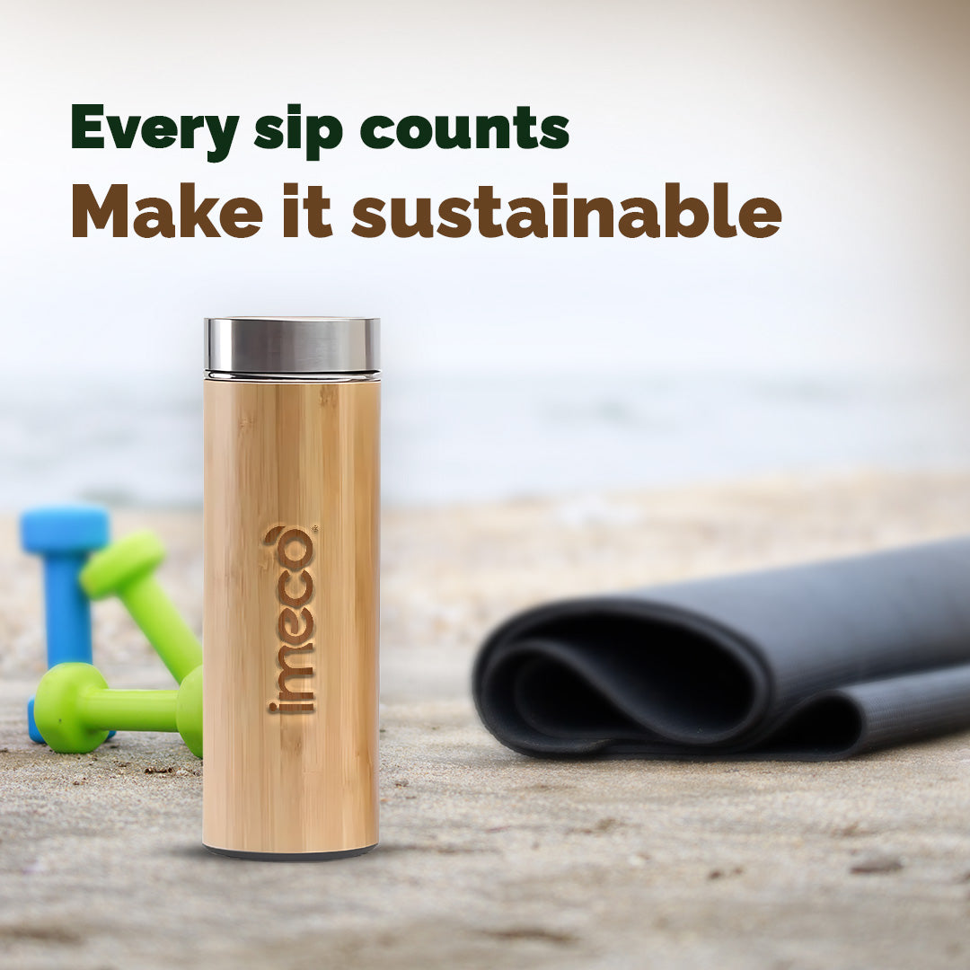 IMECO Bamboo Flat lid water bottle with 'imeco' branding on a wooden surface with fitness equipment in the background.