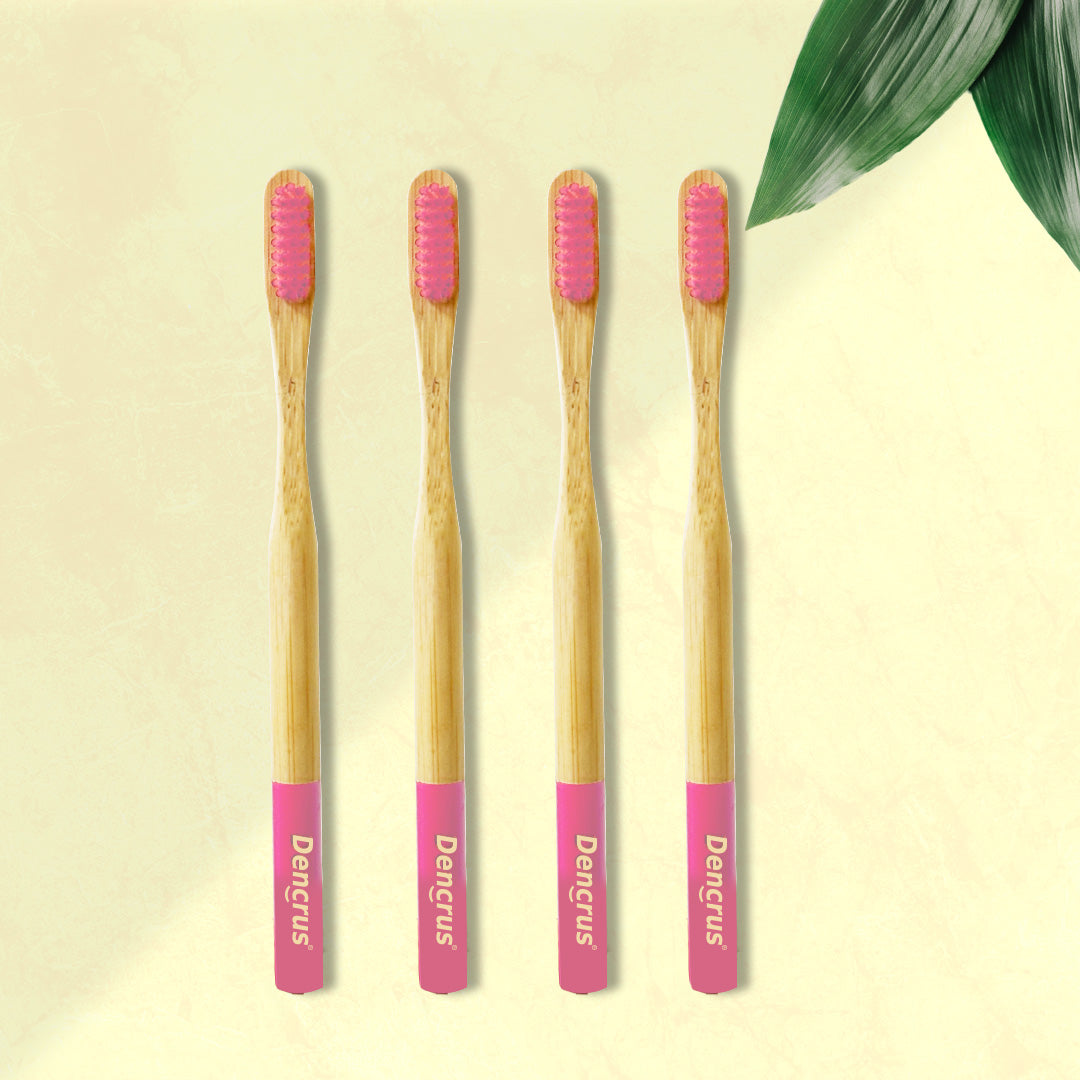 Four ORBY Plus bamboo toothbrushes with pink bristles and ergonomic handles, displayed on a neutral background with a green leaf to the side.