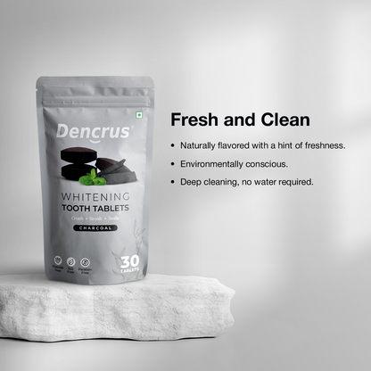 A package of Dencrus whitening tooth tablets with charcoal flavor displayed on a white stone with a white background