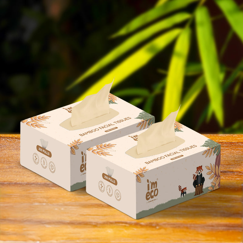 2 boxes of bamboo facial tissues are placed on a wooden table with green leaves in the background.