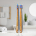 Two bamboo toothbrushes with blue and red bristles, with 'Dencrus' branding placed on bathroom counter.