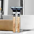 2 bamboo razors are placed together beside a towel. 
