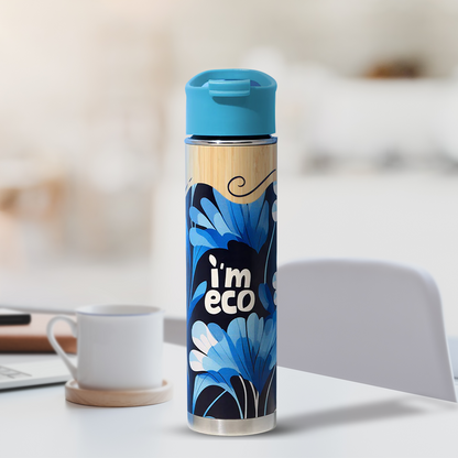 A bamboo printed water bottle with an IMECO label and blue cap is placed on a table next to a white mug and a note.