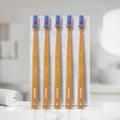 Five bamboo toothbrushes with blue and red bristles that has 'Dencrus' branding labels, placed in front of a white slab.