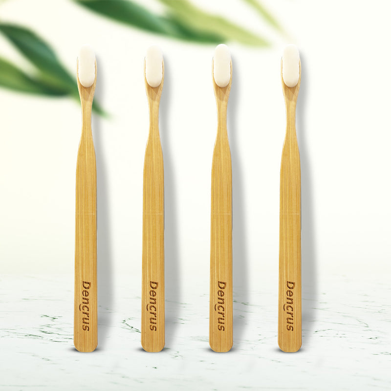 Four NANO bamboo toothbrushes with white bristles standing upright on a wooden surface, with the brand name 'Dencrus' visible on the handle.