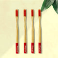 Four Dencrus ORBY Plus Red bamboo toothbrushes with red bristles and green and white branding on the handle, displayed on a beige background with a green leaf to the side.