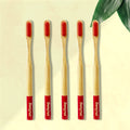 Five Dencrus RED ORBY Plus bamboo toothbrushes with red bristles and green and white branding on the handle, displayed on a beige background with a green leaf to the side.