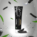 A tube of Dencrus Whitening Toothpaste with charcoal particles visible, presented against a black background with water droplets and leaves accents to highlight its natural and organic qualities.