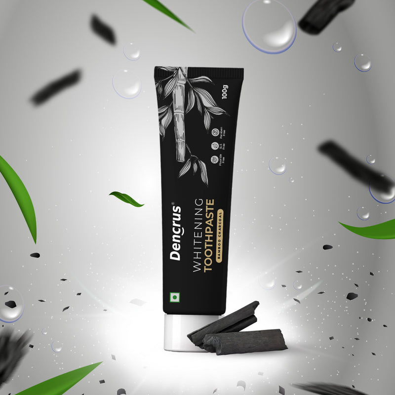 A tube of Dencrus Whitening Toothpaste with charcoal particles visible, presented against a black background with water droplets and leaves accents to highlight its natural and organic qualities.