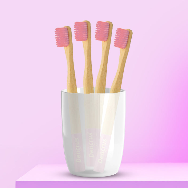 Four pink ORBY Kids bamboo toothbrushes with round handles, placed in a white cup against a pink background.