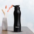 A black IMECO ECO CURVE stainless steel water bottle with a flip-top lid, branded with 'imeco', presented on a sandy surface.