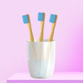 Three ORBY Kids bamboo toothbrushes with blue bristles standing upright in a white cup, set against a pink background.