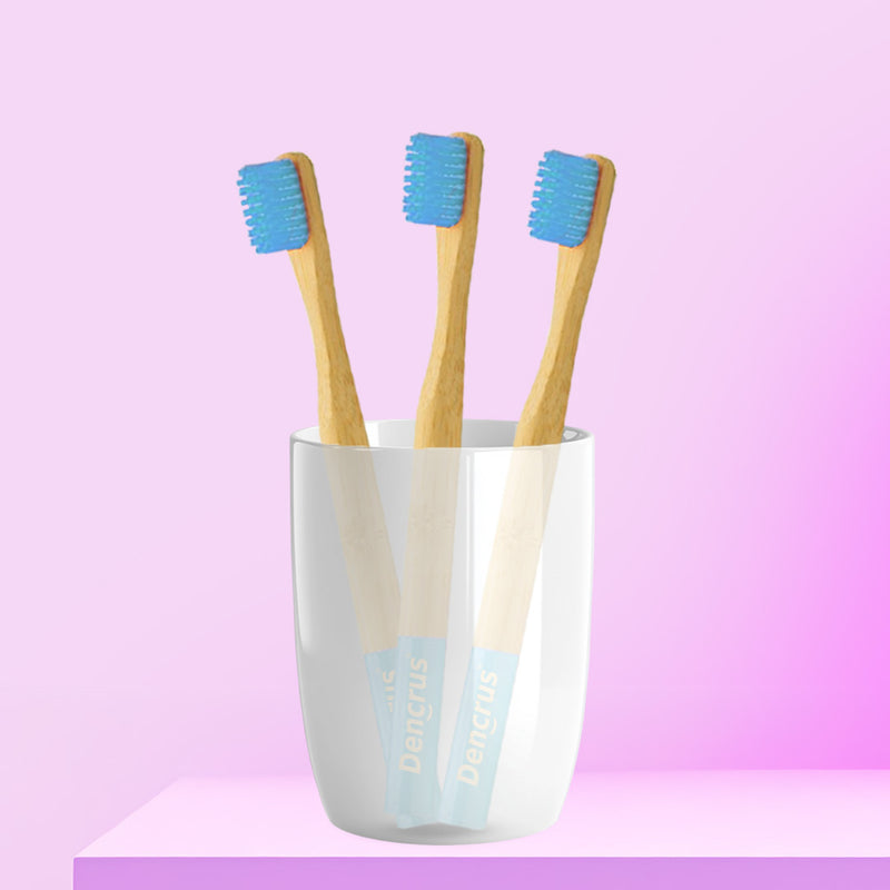 Three ORBY Kids bamboo toothbrushes with blue bristles standing upright in a white cup, set against a pink background.