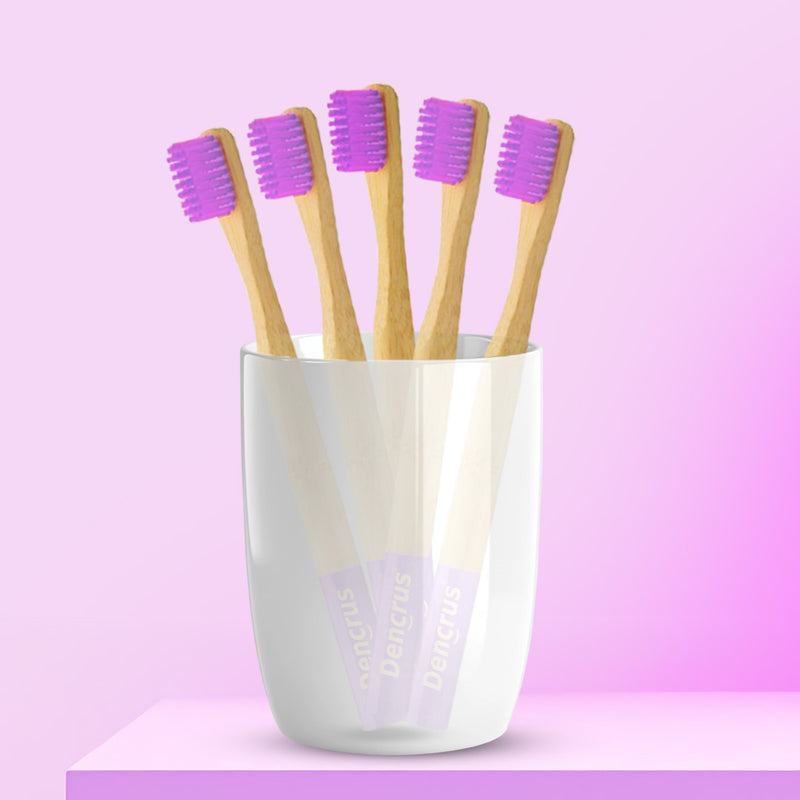Five ORBY Kids bamboo toothbrushes with lavender bristles standing upright in a white cup, set against a pink background.