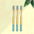 Three ORBY Plus bamboo toothbrushes with blue bristles and bamboo handles, displayed on a beige background with a green leaf to the side.