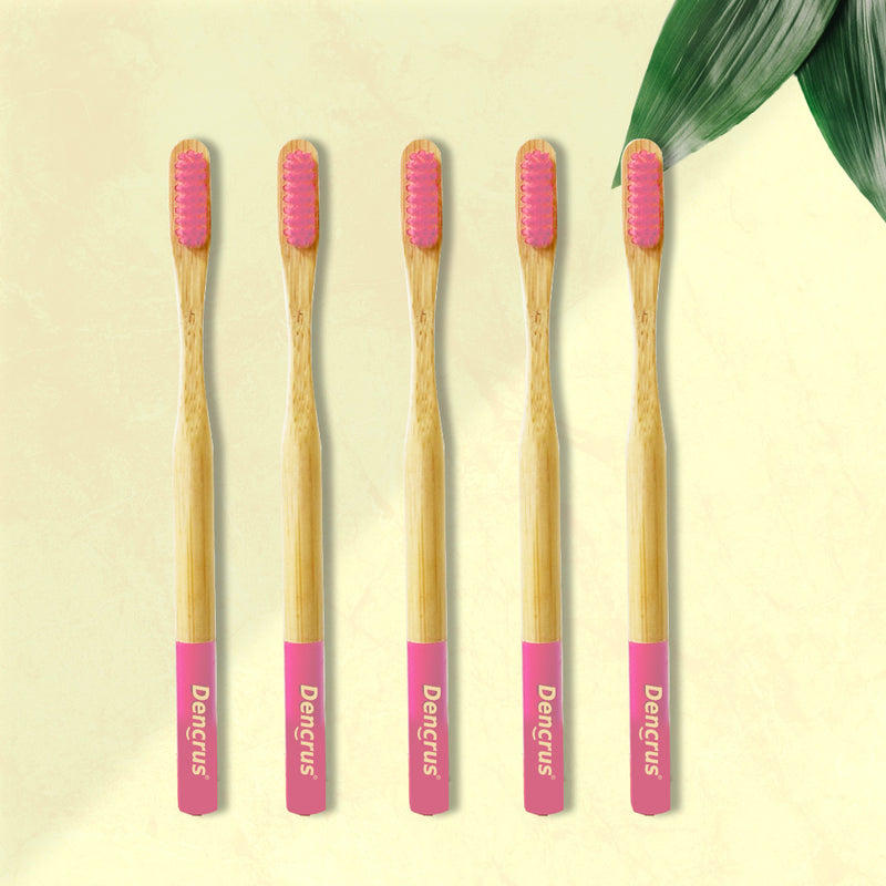 Five ORBY Plus bamboo toothbrushes with pink bristles and ergonomic handles, displayed on a neutral background with a green leaf to the side.