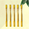 Five ORBY Plus yellow bamboo toothbrushes with ergonomic handles, displayed on a beige background with a green leaf to the side.