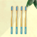Four ORBY Plus bamboo toothbrushes with blue bristles and bamboo handles, displayed on a beige background with a green leaf to the side.