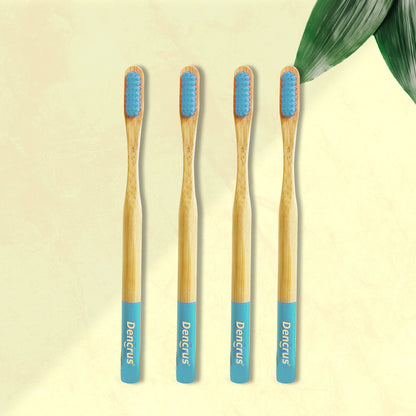 Four ORBY Plus bamboo toothbrushes with blue bristles and bamboo handles, displayed on a beige background with a green leaf to the side.