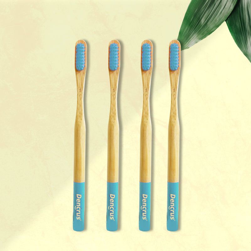 Four ORBY Plus bamboo toothbrushes with blue bristles and bamboo handles, displayed on a beige background with a green leaf to the side.
