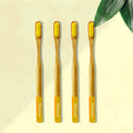 Four ORBY Plus yellow bamboo toothbrushes with ergonomic handles, displayed on a beige background with a green leaf to the side.