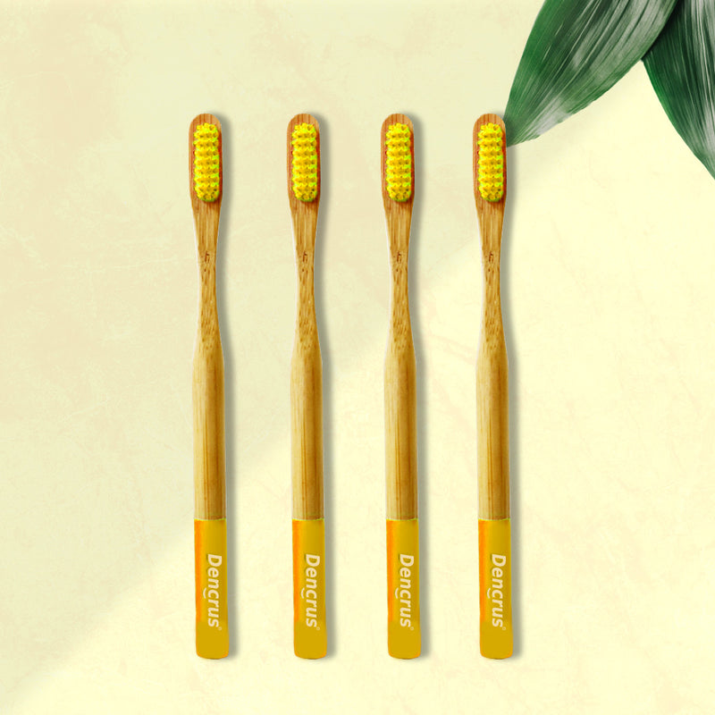 Four ORBY Plus yellow bamboo toothbrushes with ergonomic handles, displayed on a beige background with a green leaf to the side.