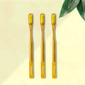 Three ORBY Plus yellow bamboo toothbrushes with ergonomic handles, displayed on a beige background with a green leaf to the side.