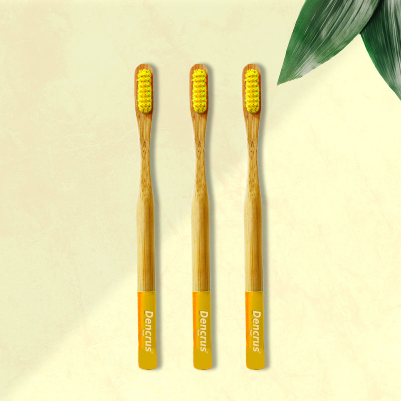 Three ORBY Plus yellow bamboo toothbrushes with ergonomic handles, displayed on a beige background with a green leaf to the side.