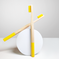 Two ORBY Plus yellow bamboo toothbrush placed on a round white block against a white background 